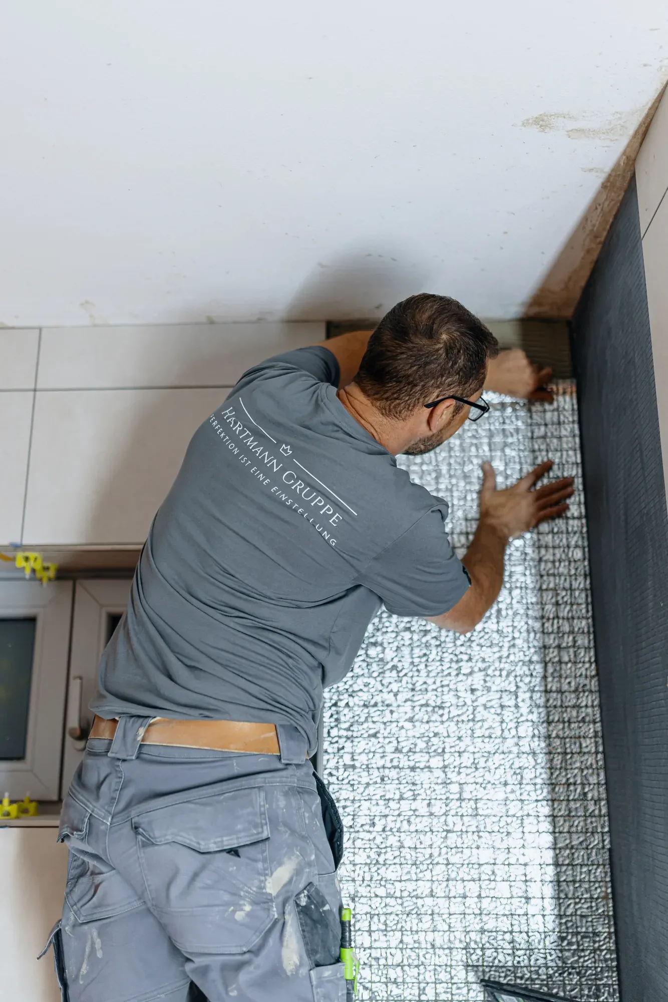 Fliesenleger der Hartmann Gruppe drückt einen Mosaikstreifen an die Wand einer Dusche