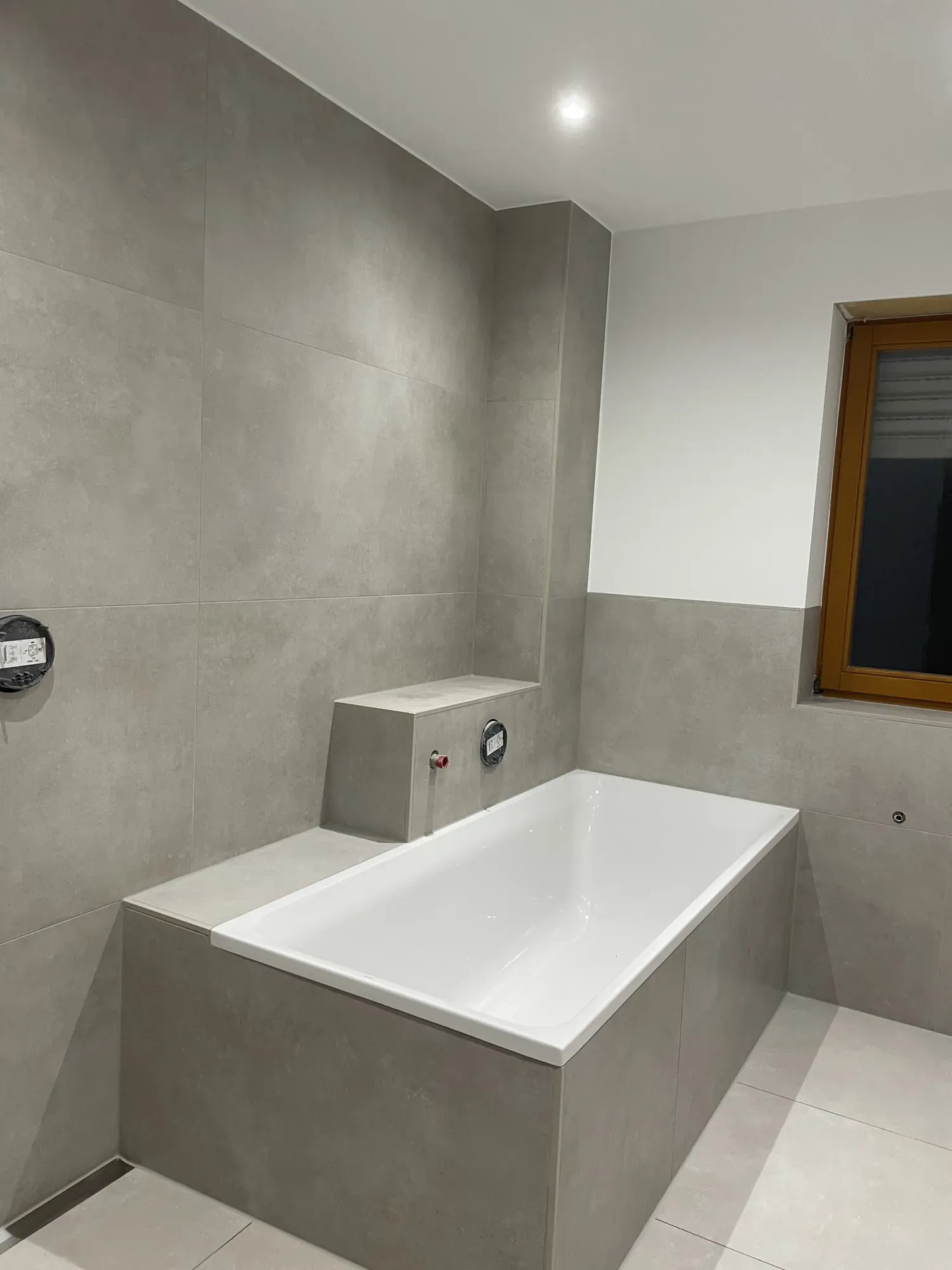 Badewanne mit gefliester Ablage in Betonoptik, Fenster mit Holzrahmen
