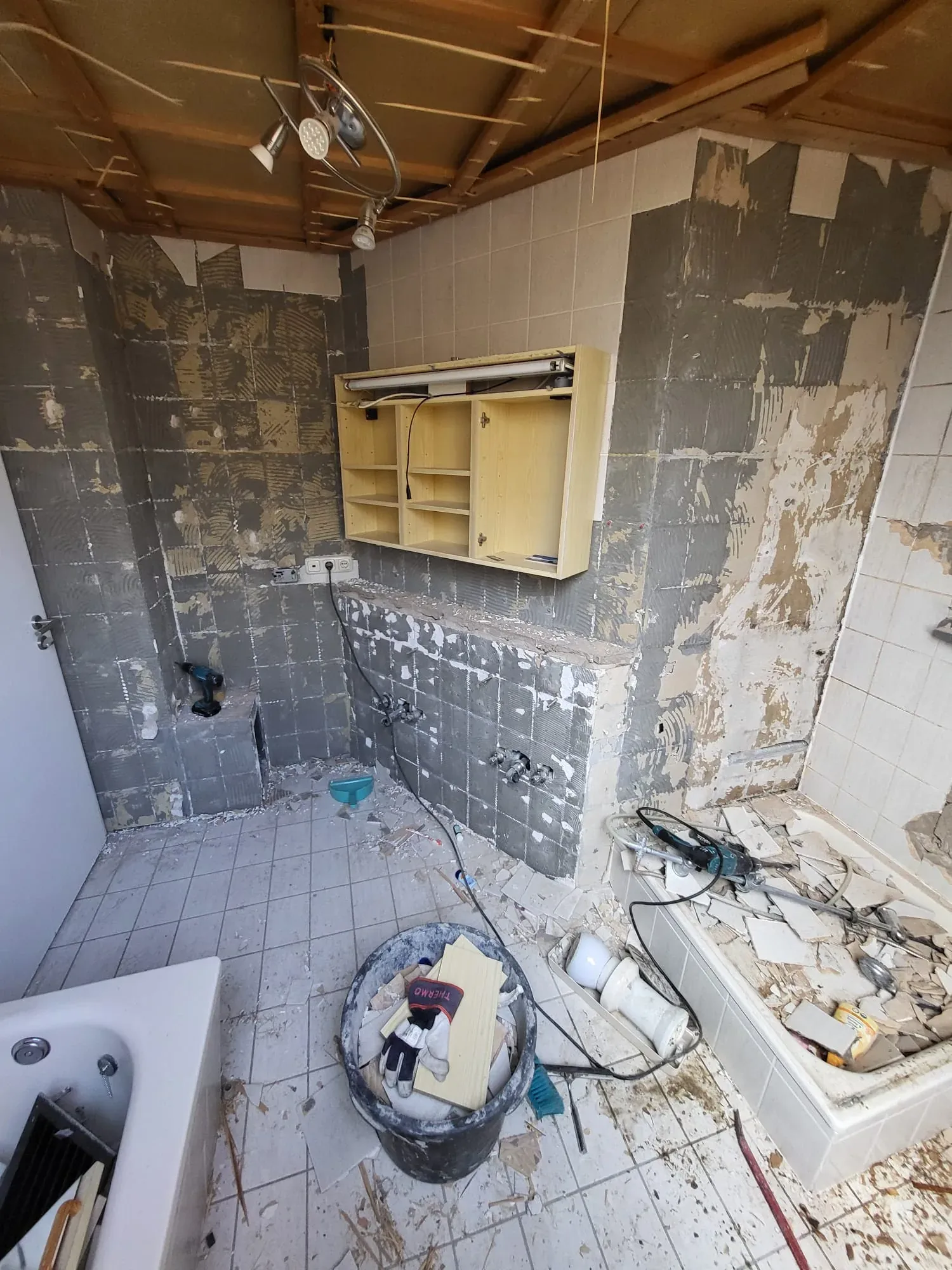 Altes Dachbad im Rückbau mit hellen Fliesen, Spiegelschrank und freigelegter Decke
