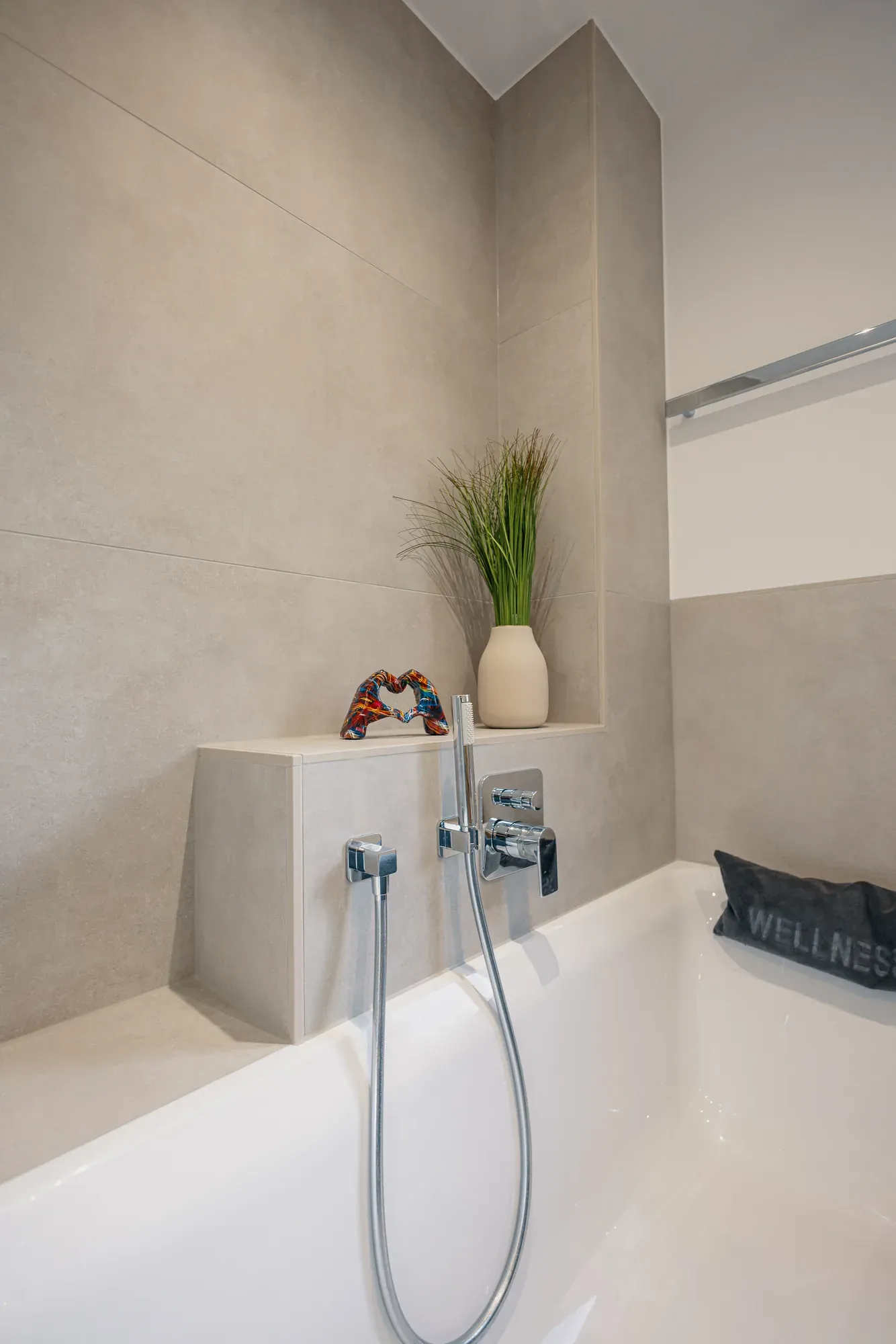 Badewanne mit gefliester Ablage in Betonoptik und Handbrause