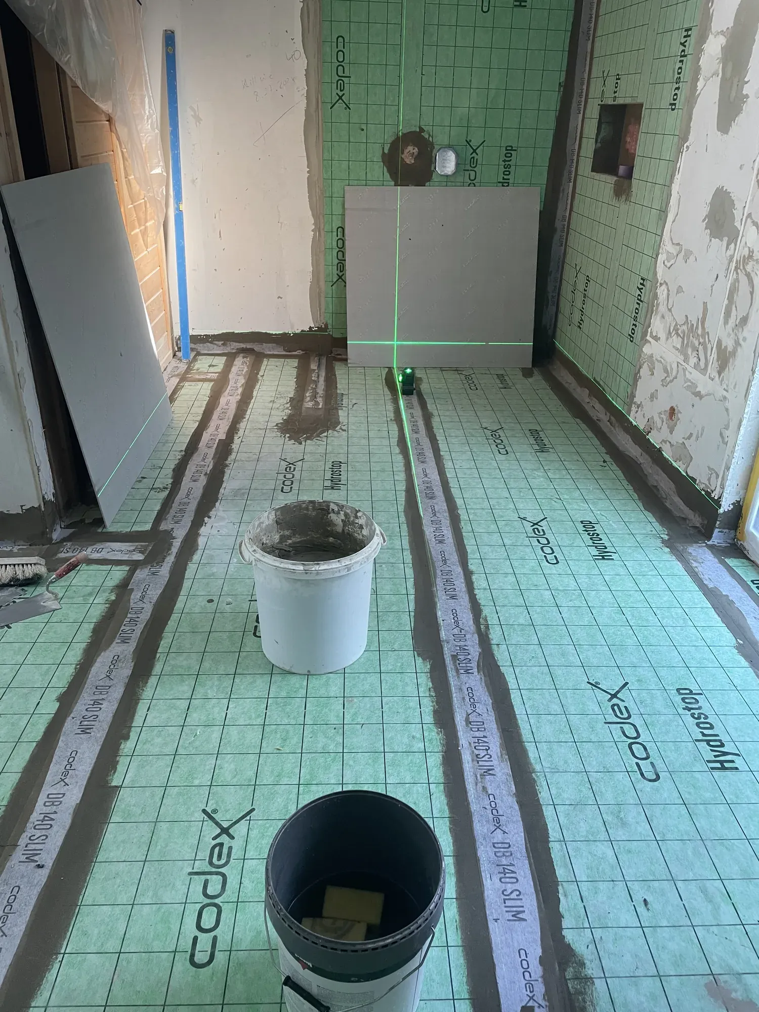 Abgedichteter Boden in einem Bad vor dem Belag, eine Fliese lehnt an der Wand