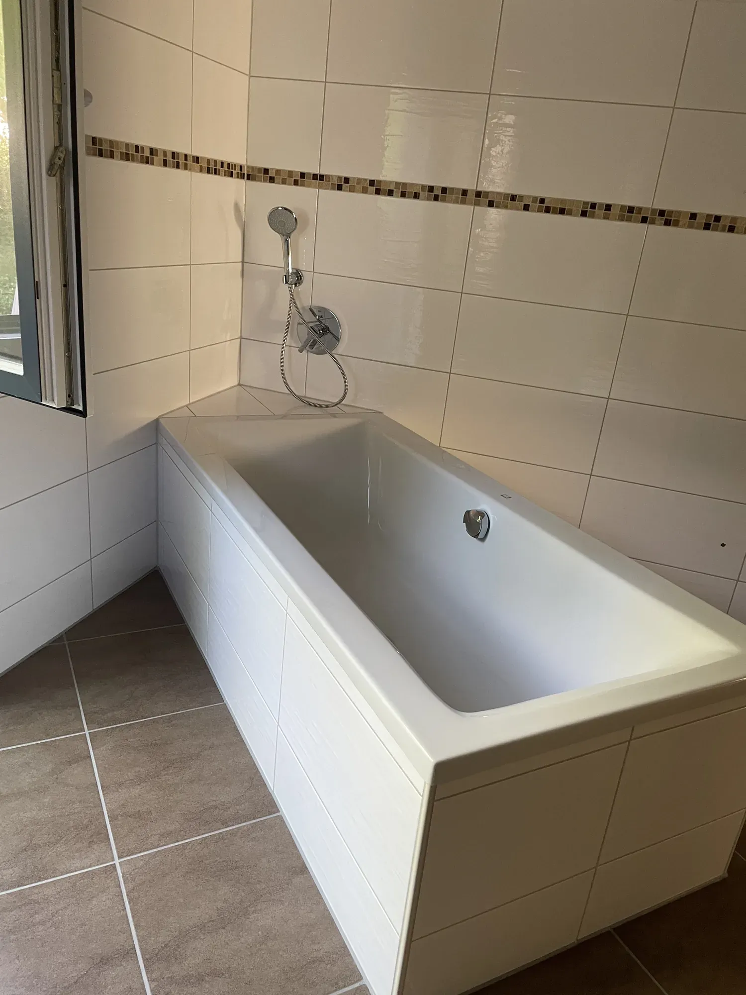 Weiße Badewanne mit weißen Wandfliesen und Mosaikbordüre