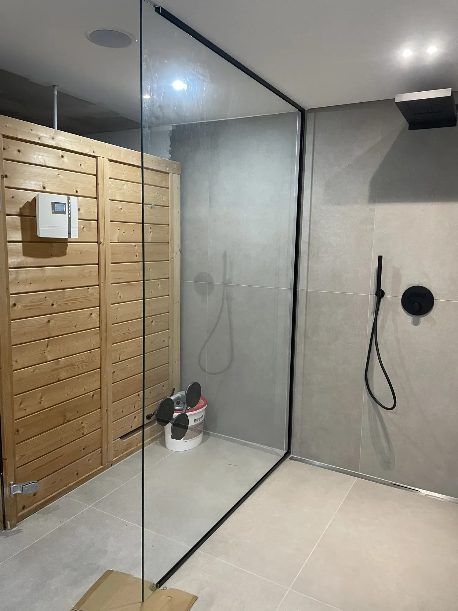 Fertige Glasdusche neben der Sauna mit grauen Großformatfliesen