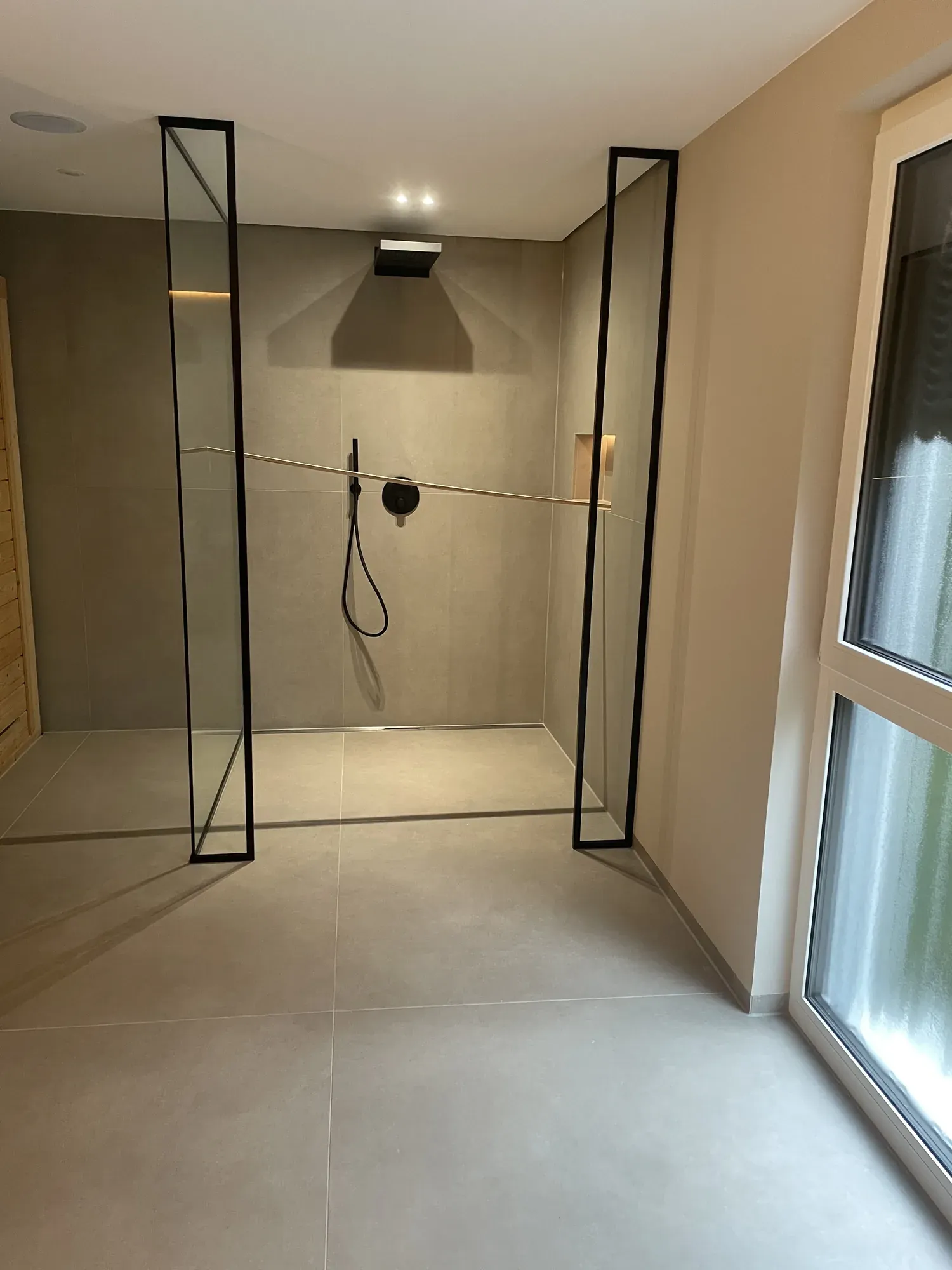Walk-in-Dusche mit schwarzen Glasrahmen und großformatigen Bodenfliesen
